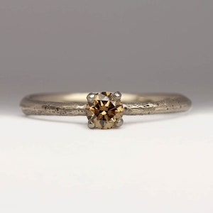 May include: A delicate gold ring with a textured band and a single brown diamond in the center.