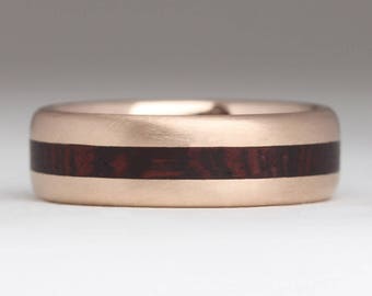 May include: A rose gold wedding band with a dark wood inlay.