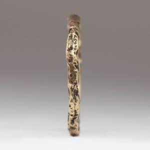 May include: A gold-toned ring with a textured, organic-looking design. The ring is made of metal and has a rough, uneven surface.