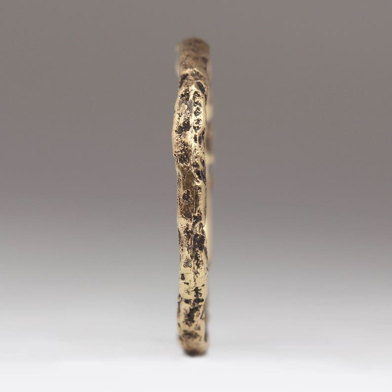 May include: A gold-toned ring with a textured, organic-looking design. The ring is made of metal and has a rough, uneven surface.