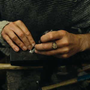 May include: A person's hands working on a piece of metal with a tool. The person is wearing a ring on their finger.