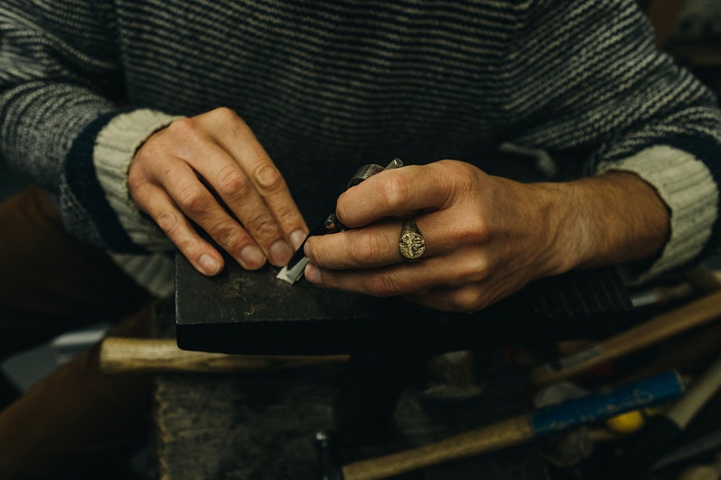 May include: A person's hands working on a piece of metal with a tool. The person is wearing a ring on their finger.