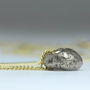 Puede incluir: Un collar con un colgante de plata en forma de coraz&oacute;n irregular y texturizado. El collar est&aacute; hecho de una fina cadena dorada.