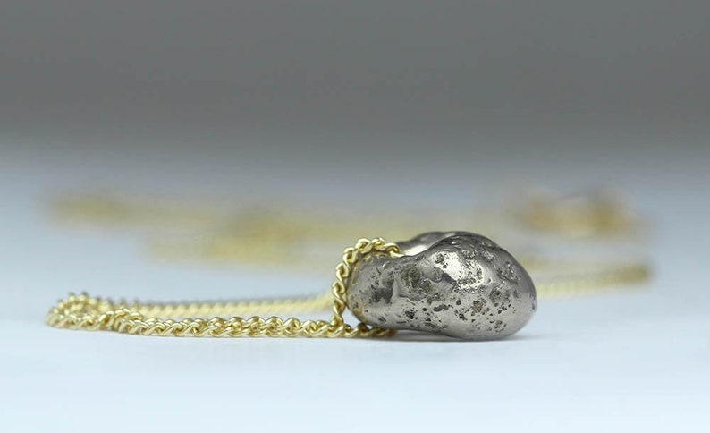 Puede incluir: Un collar con un colgante de plata en forma de coraz&oacute;n irregular y texturizado. El collar est&aacute; hecho de una fina cadena dorada.