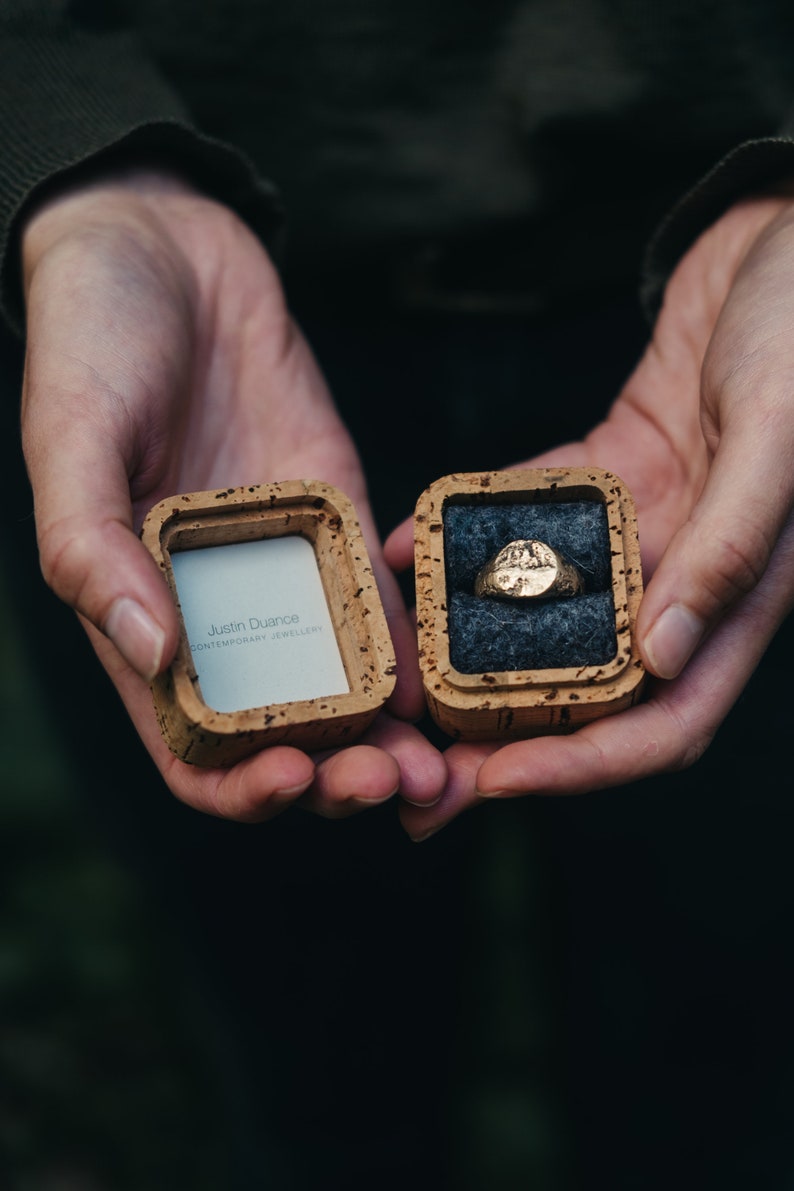 May include: Two small wooden boxes, one with a gold ring inside and the other with the text "Justin Duance CONTEMPORARY JEWELLERY".