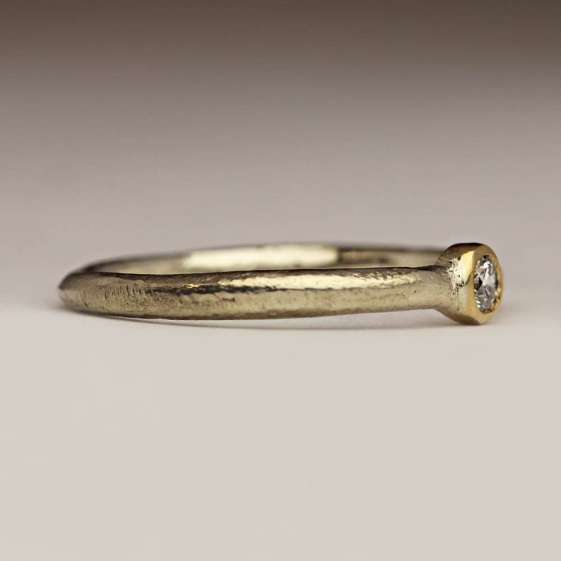 May include: A simple silver band ring with a small round diamond set in a gold bezel.