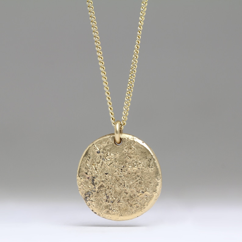May include: A gold chain necklace with a round, textured pendant.