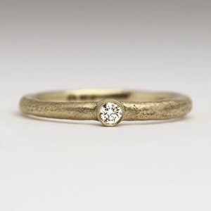 May include: A simple gold band ring with a single, small, round diamond set in the center.
