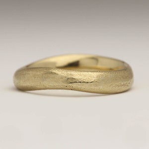 May include: A gold-colored ring with a textured surface. The ring has a smooth, rounded shape with a slightly irregular band. The ring appears to be made of solid gold and is likely a wedding band or fashion ring.