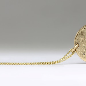 May include: A gold chain necklace with a round, textured pendant. The pendant has a rough, hammered finish.