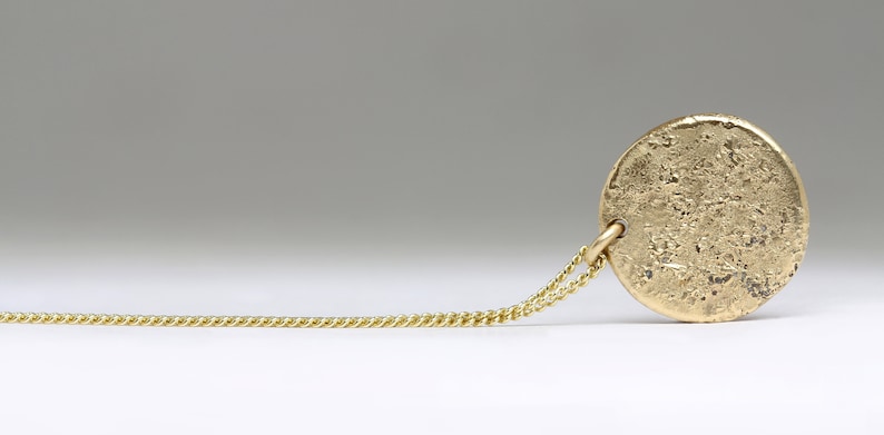 May include: A gold chain necklace with a round, textured pendant. The pendant has a rough, hammered finish.