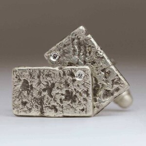 May include: A pair of silver cufflinks with a textured finish and small clear stones set in the center of each cufflink.