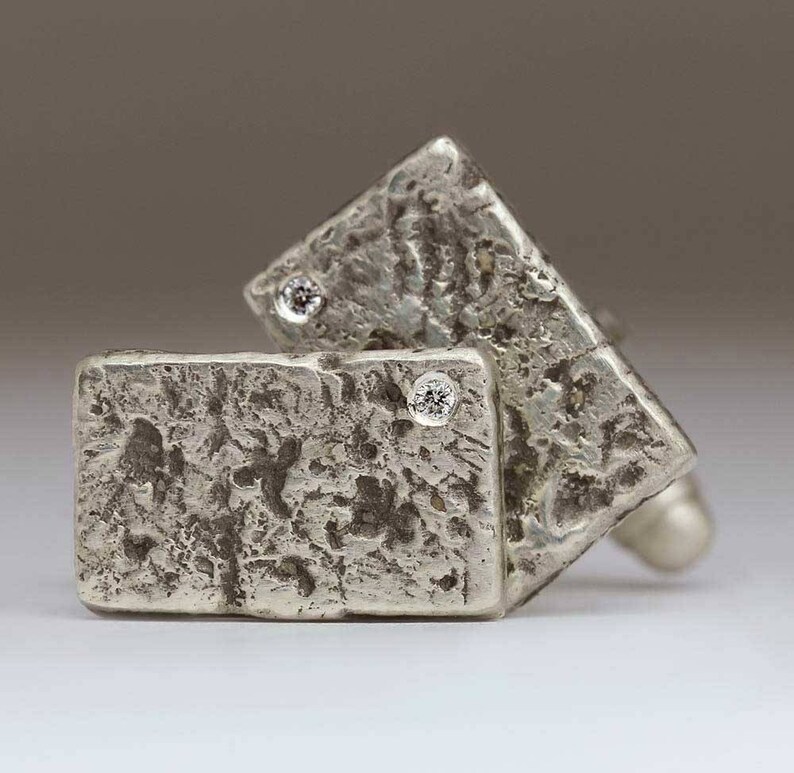 May include: A pair of silver cufflinks with a textured finish and small clear stones set in the center of each cufflink.