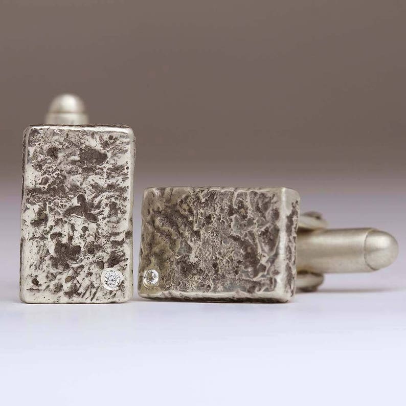 May include: A pair of silver cufflinks with a textured finish and a small diamond set in each.