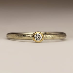 May include: A simple silver band ring with a single round diamond set in a gold bezel.