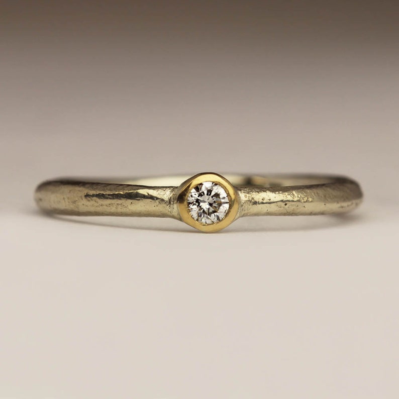 May include: A simple silver band ring with a single round diamond set in a gold bezel.