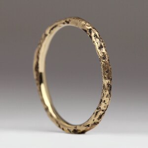 May include: A gold ring with a textured, hammered finish. The ring is simple and elegant, with a rustic look.
