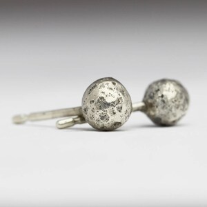 Puede incluir: Un par de pendientes de plata con una superficie texturizada, similar a la luna.