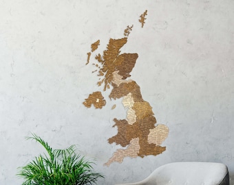 May include: A wooden map of the United Kingdom with each county outlined in a different shade of brown. The map is hanging on a gray wall above a gray armchair and a small wooden table with books on it.