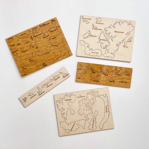 May include: Four wooden puzzle pieces, each depicting a different island with numbered outlines. The pieces are on a white surface.