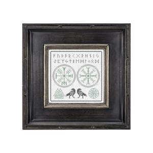 Puede incluir: Un bordado en blanco y negro enmarcado con hilo verde que representa dos cuervos, un Vegvisir, una rosa de los vientos y las runas del Elder Futhark. El marco es negro con un borde plateado.