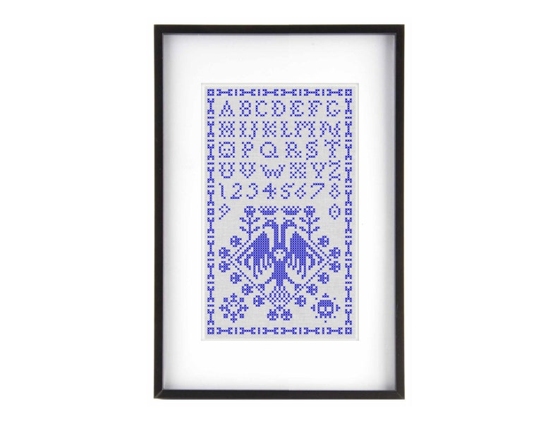 May include: Framed cross-stitch sampler with a black frame. The design features a blue alphabet, numbers, and decorative elements, including birds. The sampler is a traditional craft piece, perfect for home decor.