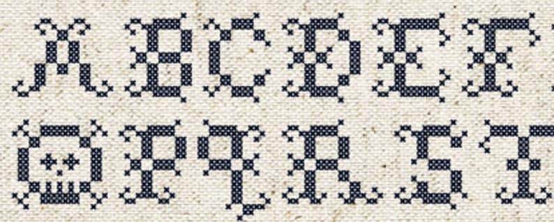 May include: Close-up of a cross-stitch alphabet sampler. The letters A through T are displayed in a dark blue color against a beige fabric background. The cross-stitch design has a decorative, ornate style.