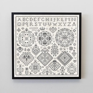 May include: Framed cross-stitch sampler with a black frame. The design features skulls, crowns, and geometric patterns in gray and white. The alphabet and the year 2016 are also included in the design. The overall theme is gothic and macabre.