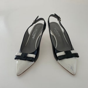 May include: A pair of black and white patent leather slingback heels with a bow detail. The heels are by the brand "MARIPE" and have a small heel.