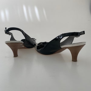 May include: A pair of black patent leather slingback heels with a white platform and a brown wooden heel.