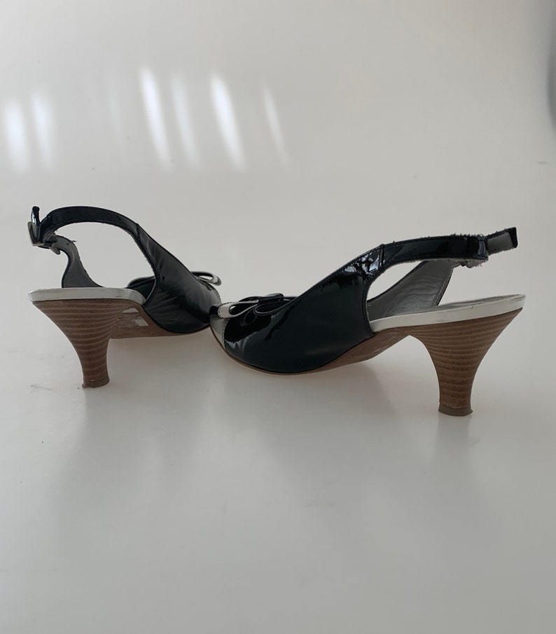 May include: A pair of black patent leather slingback heels with a white platform and a brown wooden heel.
