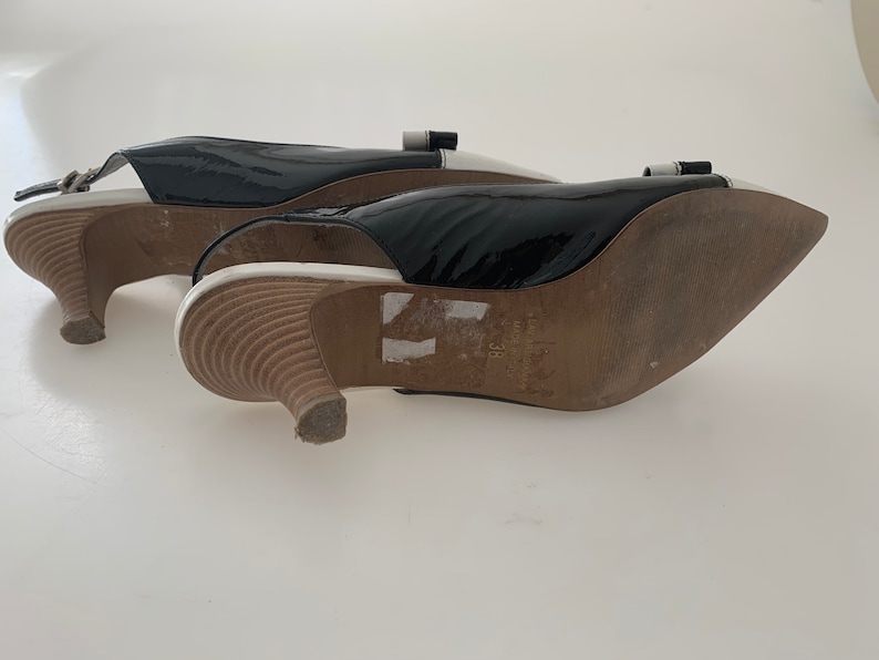 May include: A pair of black patent leather heeled shoes with white trim and a buckle detail. The shoes have a pointed toe and a low heel.