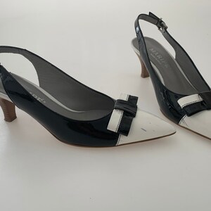 May include: A pair of black and white patent leather slingback heels with a bow detail. The heels are approximately 3 inches tall.