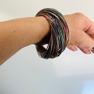 Peut inclure: Un bracelet composé de plusieurs bracelets fins en métal, superposés. Les bracelets sont de couleur argentée, dorée, cuivrée et bleue.