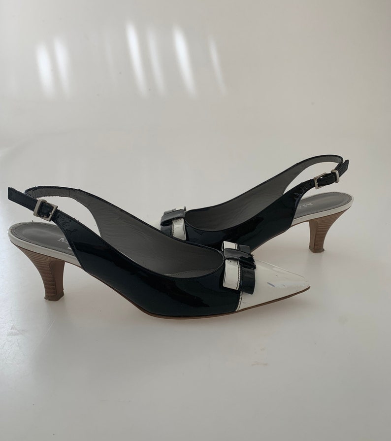 May include: Black and white patent leather slingback heels with a bow detail on the toe.
