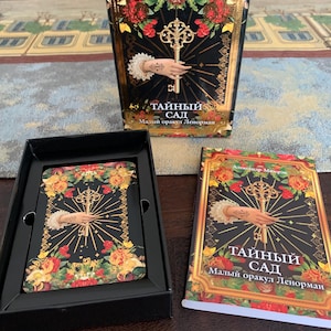 May include: A deck of oracle cards titled "Тайный Сад" featuring a black background with red and yellow roses, a gold key held by a hand, and a matching guidebook. The box and cards display the text "Александр Мюсрэк" and "Малый оракул Ленорман".