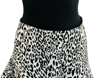 May include: A short skirt featuring a high-contrast black and white leopard print pattern. The garment has a fitted waistband and a flared, ruffled hemline that creates a subtle A-line silhouette. The fabric displays a consistent animal print.