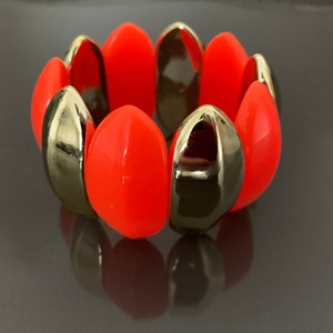 Könnte beinhalten: Ein leuchtend orangefarbenes und goldenes Armband aus ovalen Perlen. Das Armband besteht aus abwechselnden Farben von Orange und Gold.