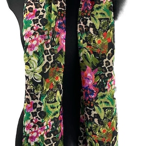 May include: A long, rectangular scarf with a floral and leopard print. The scarf is made of a lightweight fabric and features a variety of colors, including pink, green, and brown.