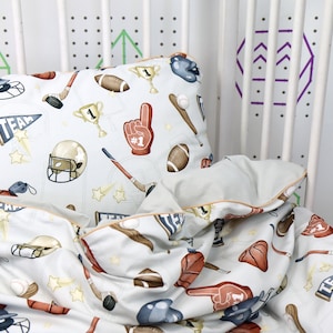 May include: A white and gray bedding set with a sports theme. The pillowcase features a pattern of baseballs, bats, hockey sticks, and other sports equipment. The bedding is made of soft, comfortable fabric and is perfect for any sports fan.