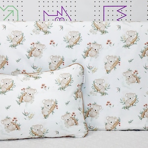 Puede incluir: Dos fundas de almohada blancas con un patrón repetido de koalas marrones en una rama con hojas verdes y pequeñas flores rojas. Las fundas de almohada tienen un ribete marrón.
