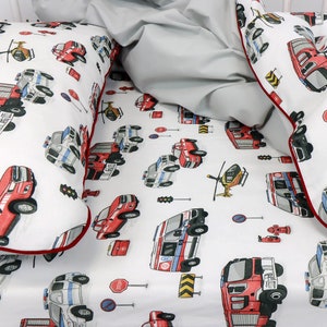 Könnte beinhalten: Weißes Kinderbettwäsche-Set mit einem sich wiederholenden Muster aus roten Feuerwehrautos, Polizeiautos, Krankenwagen, Hubschraubern und Verkehrsschildern. Der Kissenbezug und das Spannbetttuch haben eine rote Bordüre. Eine graue Decke ist ebenfalls enthalten.