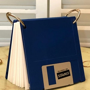 May include: A blue floppy disk binder with a white paper insert and two gold rings. The floppy disk has a silver label with the text "STAPLES IBM FORMATTED".