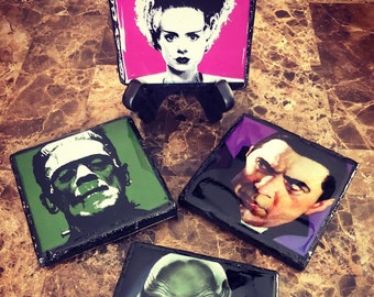 May include: Set of four square coasters featuring classic monster movie characters. The coasters include images of the Bride of Frankenstein, Frankenstein's monster, Dracula, and the Creature from the Black Lagoon. Each coaster has a black border.