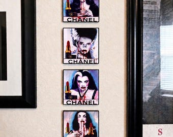 May include: A set of four square wall art tiles featuring illustrations of female figures with dark hair and red lipstick, each accompanied by a Chanel lipstick tube and the brand name CHANEL printed in black text at the bottom of each individual tile.