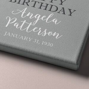 May include: A gray canvas print with the text "Happy Birthday Angela Patterson January 31, 1930" in white and black lettering.