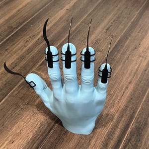 May include: A light blue plastic hand with five black metal claws attached to the fingers.