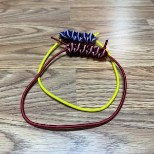 May include: Three colorful hair ties on a wooden surface. The hair ties are in shades of yellow, burgundy, and blue. The burgundy and blue hair ties have a decorative, textured design. The yellow hair tie is a simple, smooth band.