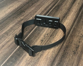 May include: A black adjustable collar with a black plastic buckle and a rectangular tag that says "BRAT" in white letters.