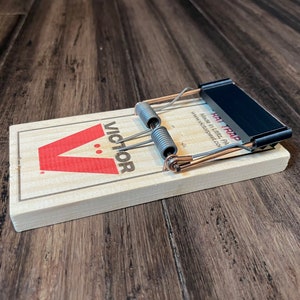 May include: A wooden Victor rat trap with a black metal bar and a spring mechanism. The trap is labeled "Rat Trap" and "Made in Lititz, PA www.victorpest.com".